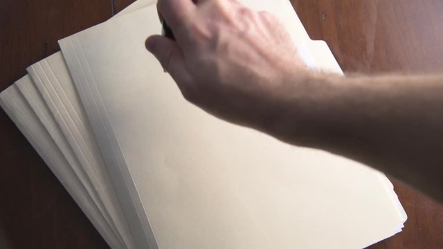 Hand stamps confidential in red on stack of folders resting on wooden table.