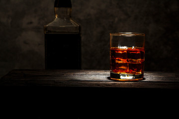Whiskey with ice or brandy in a glass and a square carafe on an old wooden background. Whiskey with...