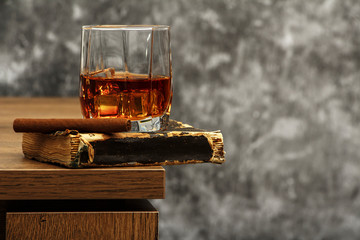 Whiskey with ice or brandy in a glass on a background of gray concrete on an old wooden table....