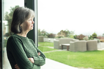 Lonely senior woman looking through window