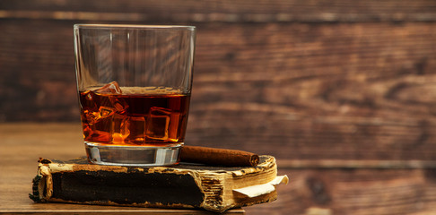 Whiskey with ice or brandy in a glass and a square carafe on an old wooden background. Whiskey with...