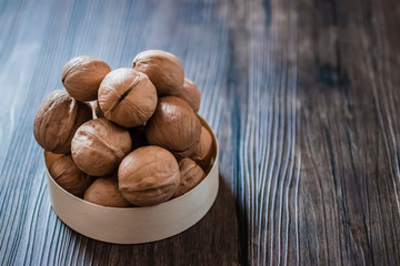 Walnuts in a brown plate on a brown wooden table.