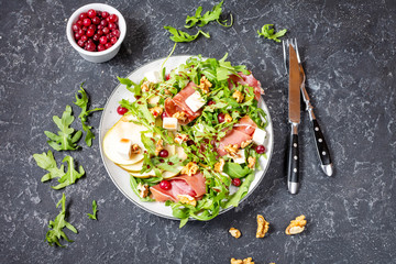 Green salad with arugula, pear, jamon and feta cheese on dark stone background. Top view.
