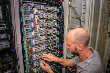  A specialist connects the wires in the server room of the data center. A man works with...