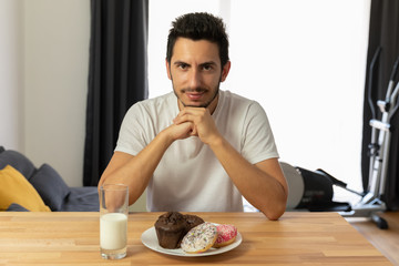 Young handsome guy sits at a table and eats donuts.