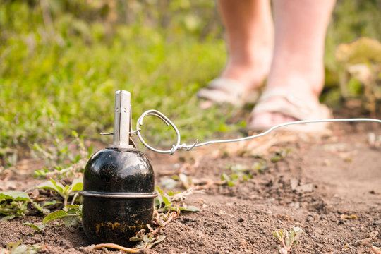 A grenade trap is on the ground. Improvised explosive device consists of a wire and a grenade tied to a ring. Female legs are in front of the mine. Selective focus