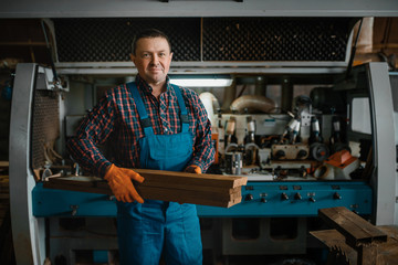 Carpenter in uniform holds boards, wood processing - obrazy, fototapety, plakaty