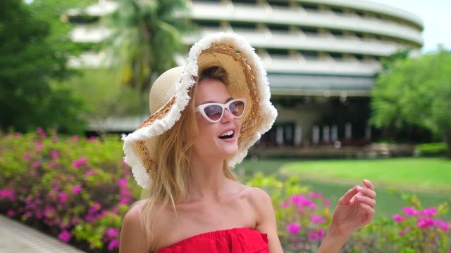 Pretty beautiful traveler woman girl in red dress, hat, sunglasses walking at luxury resort, Female tourist woman in tropical hotel. travel tourismbeach vacation happy holiday check-in slow-mo 4 K
