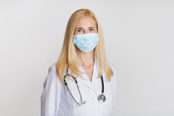 Female doctor in mask and with stethoscope on gray background