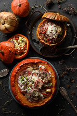 Healthy meat free food. Orange pumpkins stuffed with brown and white rice, giant couscous, mushrooms, onion and grated cheese on black background