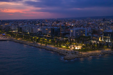 Fototapeta premium Aerial view of Limassol promenade or embankment with alley and buildings in Cyprus at night. Drone photo of mediterranean sea resort from above.