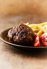 Hamburger steak with french fries and tomatoes. Brown stone background. Close up. 