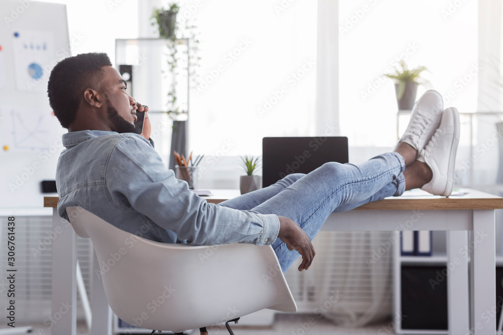 Poster lazy afro worker talking on cellphone with his feet on desk
