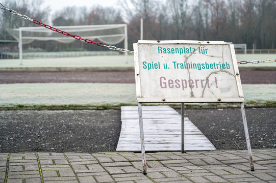Verbotsschild mit der Aufschrift "Rasenplatz für Spiel- und Trainingsbetrieb gesperrt" in deutscher Sprache vor einem Fußballplatz