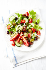 Salad with Olives, Tomatoes and Cucumber on bright wooden Background. Healthy Snack Idea. Top view. 