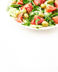 Salad with green Olives, Tomatoes, Cucumber and Rocket on bright Background. Healthy Snack Idea. Copy space.
