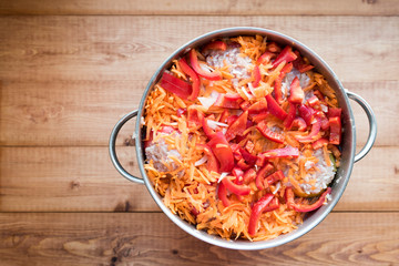 Top view of a pot with chopped fresh vegetables. A dish of stuffed peppers before cooking on the stove. Brown wood background.