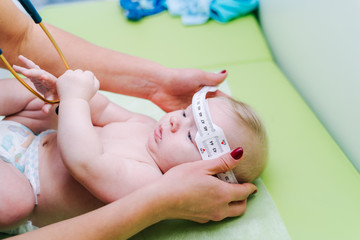 Shot of a pediatrician examining newborn baby. Doctor using measurement tape checking baby's head size. Closeup.