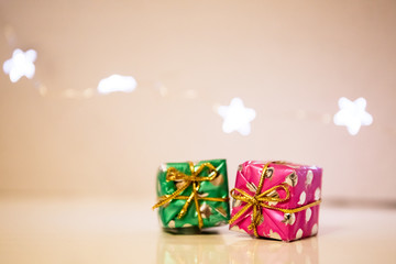 Two small gift boxes wrapped in festive Christmas paper lie on the table, and a garland of lights in the shape of stars