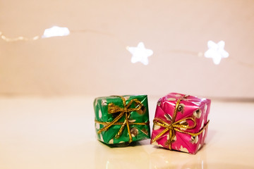 Two small gift boxes wrapped in festive Christmas paper lie on the table, and a garland of lights in the shape of stars