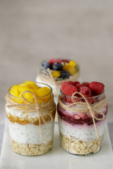 Three glass jars of yogurt pudding with сhia seeds, oats, berries and jam on a marble board. The concept of healthy eating, diet.