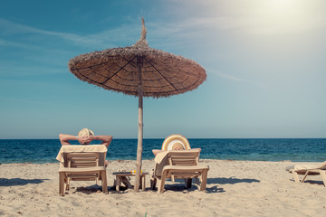 Happy European couple laying on sunbeds under straw umbrella at the tropic beach. They enjoying their vacations. - 306766435