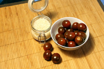 Small dark tomatoes in a white bowl and a glass jar with rice on a table