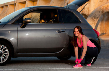 woman getting ready for sports, next to the car with fuchsia tank top, black pants and fuchsia sports shoes