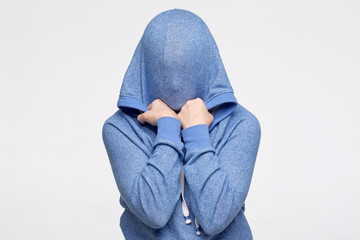 Teenager hiding her face under blue sweater being frightened and stressed