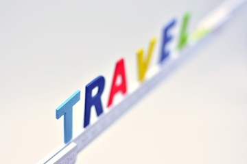 La palabra travel, hecha con letras de madera sobre un metro de carpintero blanco