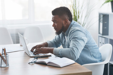 Concentrated young african worker using laptop in office