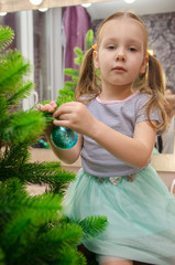 Adorable little girl decorating a Christmas tree with colorful glass baubles at home.Child decorating Christmas tree at home. Kids decorate living room and fireplace for Christmas.