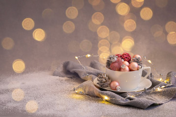 Pink christmas balls and natural cone in the white tea set on grey background, toned