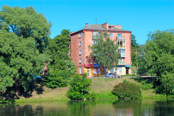 Fototapeta na wymiar Multi-storey house standing in green trees near river. Nature in city