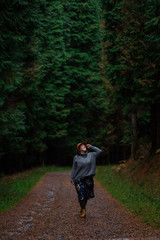 Fototapeta na wymiar beautiful young woman with hat, sweater and skirt walking on a pine forest path. Otzarreta, Basque Country, Spain