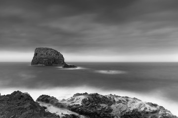 Seascape on a cloudy early evening with volcanic rocks on foreground and a large sea rock in the background, Black and White Photo, Madeira Island, Portugal