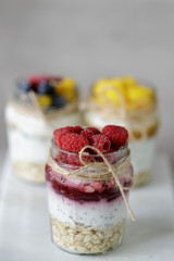Tasty and healthy: delicate yogurt pudding with сhia, raspberries, oats and jam in a glass jar on a marble вoard.