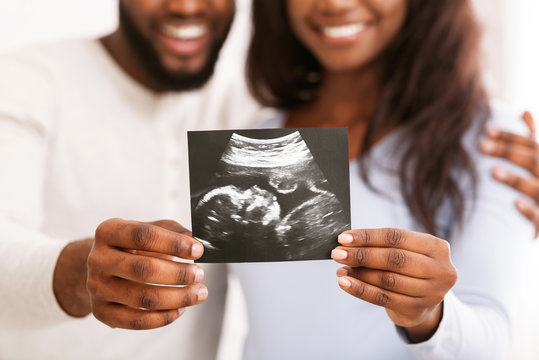 Smiling black couple holding ultrasound image, expecting baby