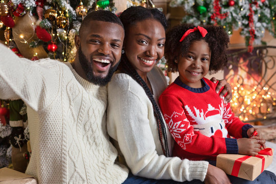 Black parents taking selfie with their little daughter near Christmas tree
