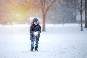 Fototapeta na wymiar A little boy in a hat and jacket laughs and rejoices in the winter snow .
