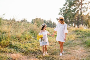 Cheerful mother and her little daughter having fun together in the summer background. Happy family in the nature background. Cute girls with colorful flowers.