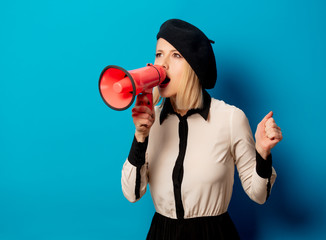 beautiful french woman in beret holds  loud-hailer on blue background
