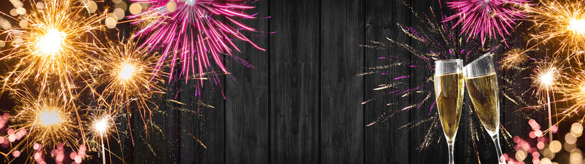 Silvester background banner panorama long- sparklers, pink golden firework, champagne glasses and bokeh lights on rustic wooden texture, with space for text
