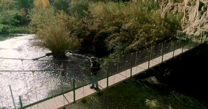 Vuelo orbital de dron de anciano con barba canosa mirando r&iacute;o en puente colgante