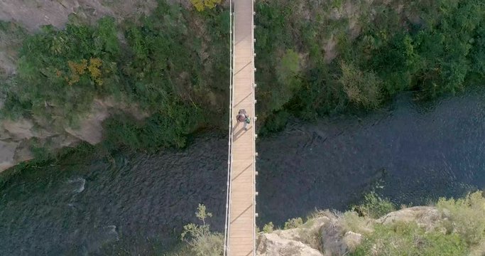 caminante de tercera edad con barba blanca cruzando un puente colgante sobre barranco y dron encima