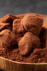 Macro chocolate truffles with cocoa in wooden plate on table on dark background.