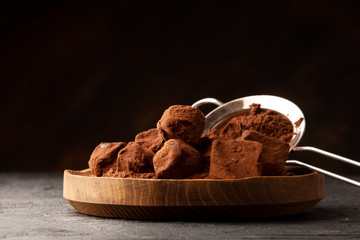 Chocolate truffles with cocoa in wooden plate on table on dark background. Copy space