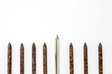 A metallic shiny sharp nail stands out in a row of old rusty nails on a white paper background.