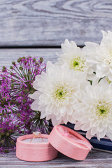 Engagement ring in box and flowers close up. Gift box with diamond ring on beautiful flowers background. Valentine holiday, marriage proposal or Birthday.