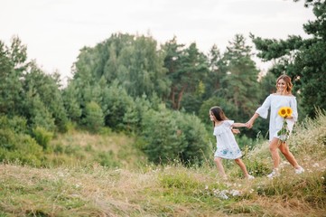 Fototapeta premium Cheerful mother and her little daughter having fun together in the summer background. Happy family in the nature background. Cute girls with colorful flowers.